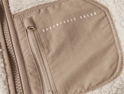 Detalje af brystlomme med tekst Adventures Ahead på Name It teddy jakke