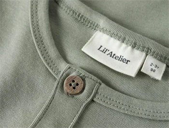 Nærbillede af halsudskæring og knapper på Lil\' Atelier t-shirt i seagrass