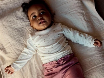 Baby iklædt Name It body i råhvid nuance med kirsebærprint