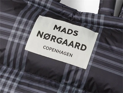 Nærbillede af logo på sort og hvid ternet puffertaske fra Mads Nørgaard