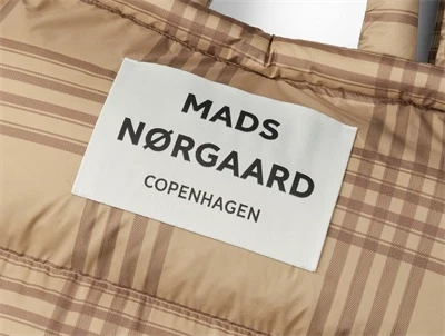 Nærbillede af logo på ternet puffertaske i beige og brun fra Mads Nørgaard