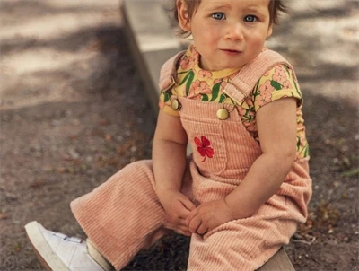 Barn iført peachfarvede fløjlsdungarees fra Mini Rodini med firkløverbroderi
