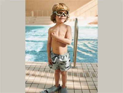 Barn iført Liewood Aiden badeshorts i shark med hajprint ved pool